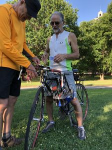 A white man wearing a cap helps a white man with a beard and sunglasses check in his road bicycle for valet parking in Bushnell Park.