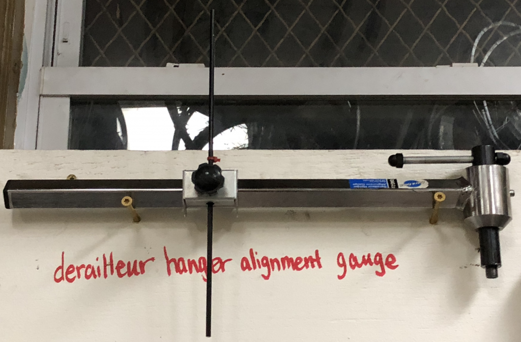 A derailleur hanger alignment gauge, a bicycle repair tool, hanging on a wall